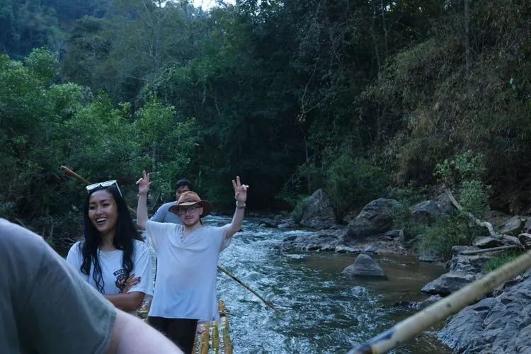 Two sprint participants laughing and waving while bamboo rafting on a jungle river